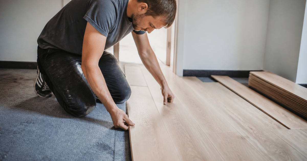 Ouvrier posant planches bois sur moquette grise existante