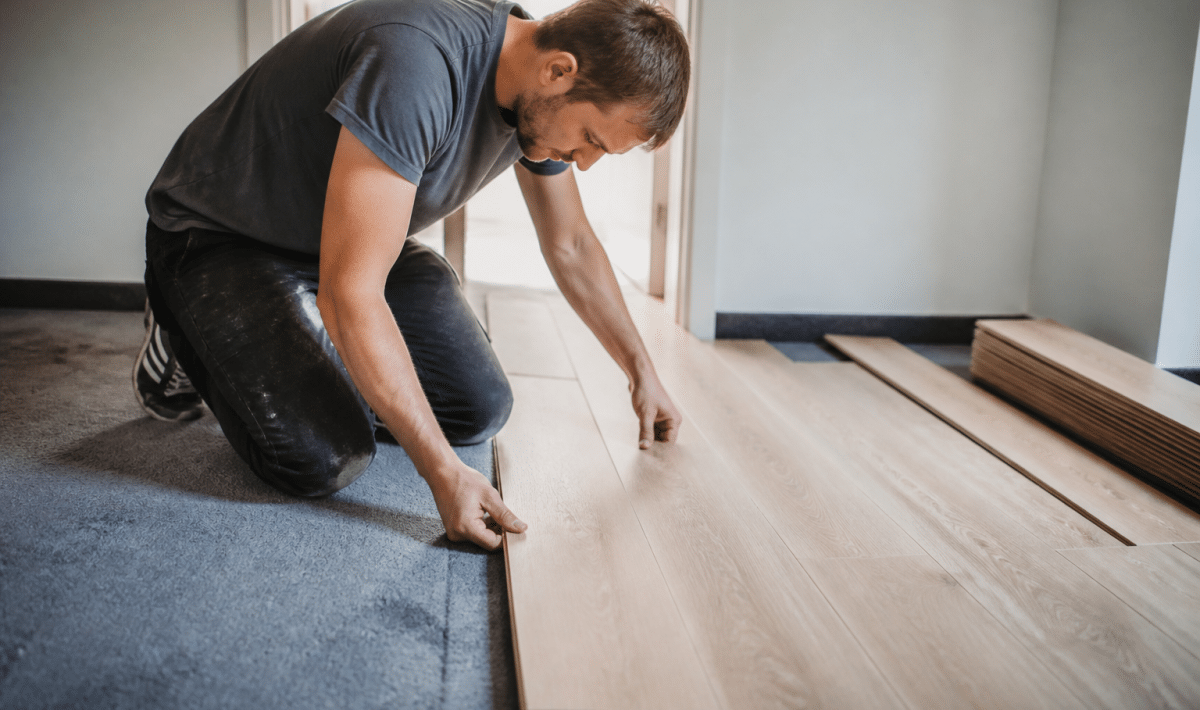 Ouvrier posant planches bois sur moquette grise existante