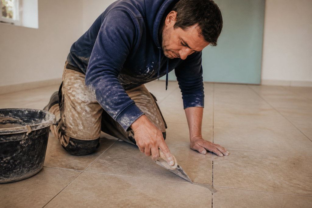 Ouvrier comblant joints creux carrelage avec spatule