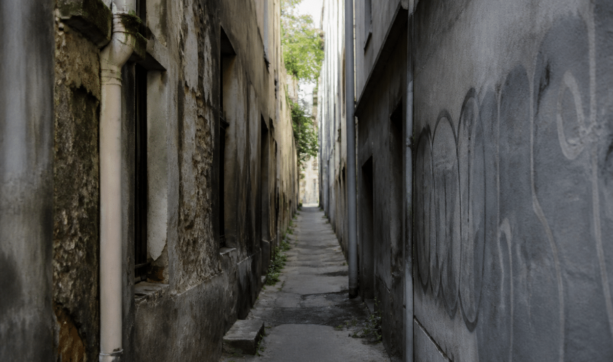 rue étroite avec immeubles dégradés et graffitis sur murs gris