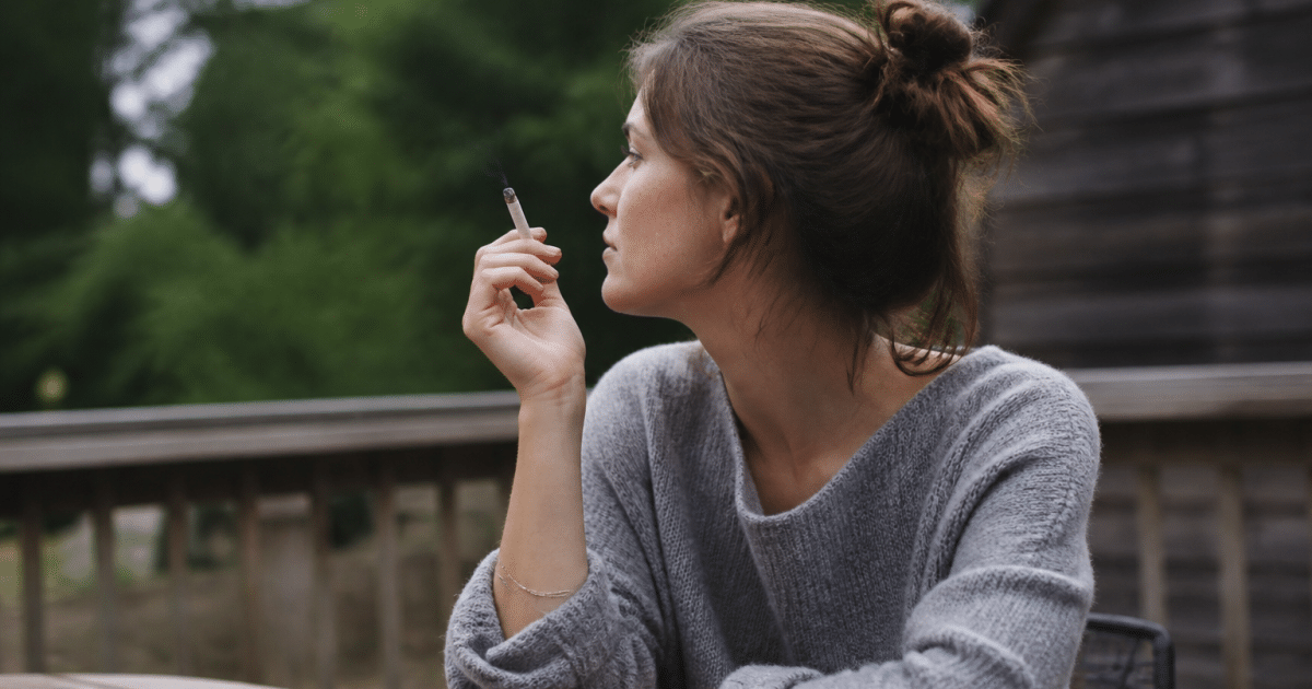 Personne assise a une table exterieure tenant une cigarette allumee