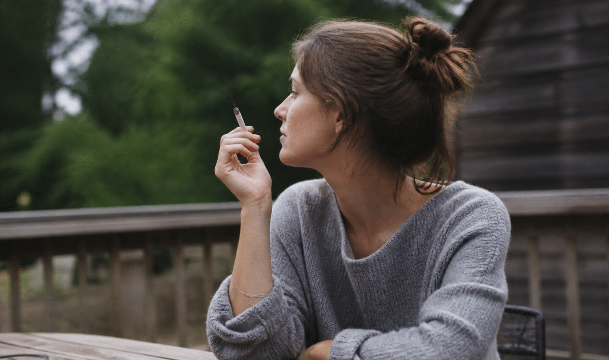 Personne assise a une table exterieure tenant une cigarette allumee