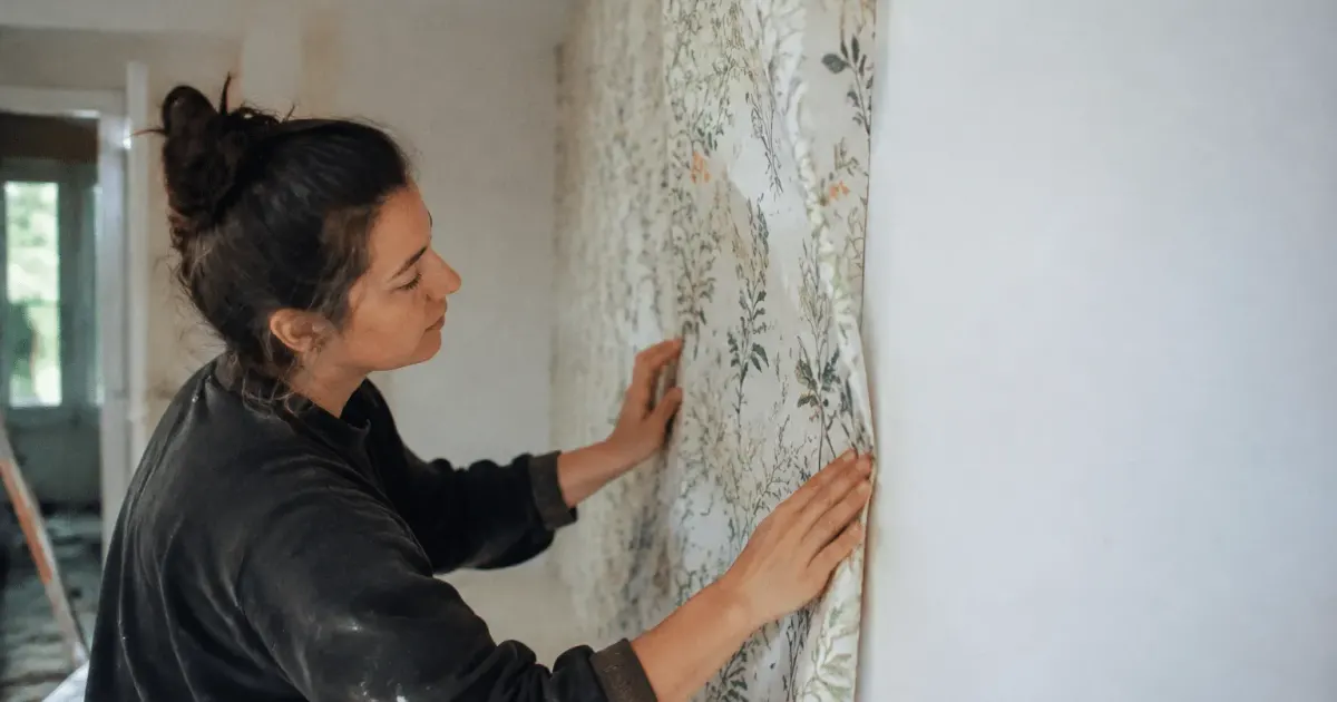main appliquant papier peint sur angle convexe de mur blanc